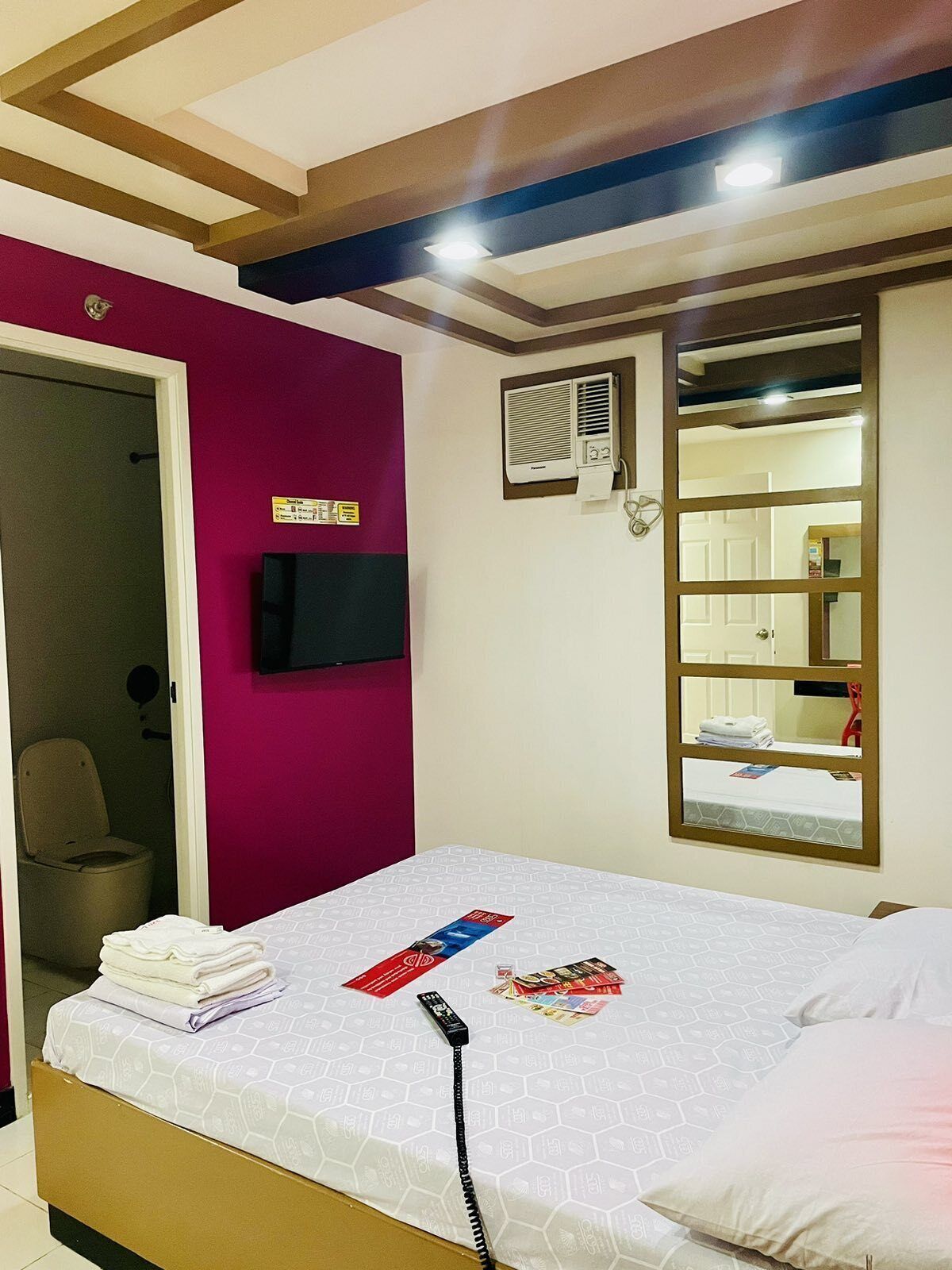 Une chambre d’hôtel équipée d’un lit, d’un téléviseur fixé au mur, d’un appareil de climatisation et d’une porte donnant accès à une salle de bain.