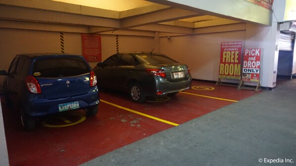 A parking garage with two cars parked in designated spaces. There are signs indicating parking rules and a pick and drop area. - Hotel Sogo Dau (Mabalacat City)