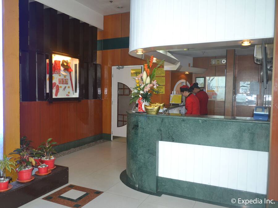 A reception area with a green counter, potted plants, and a sign indicating a 24-hour service.