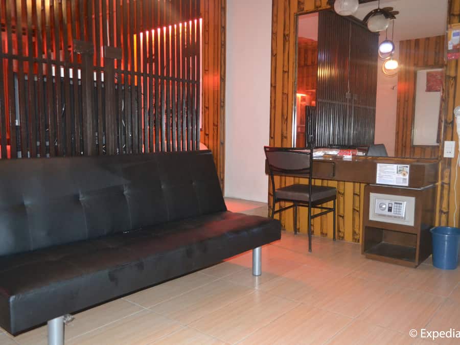 Une pièce moderne avec un canapé en cuir noir, un bureau en bois et une chaise. On y trouve une poubelle bleue et un clavier de sécurité sur le bureau.