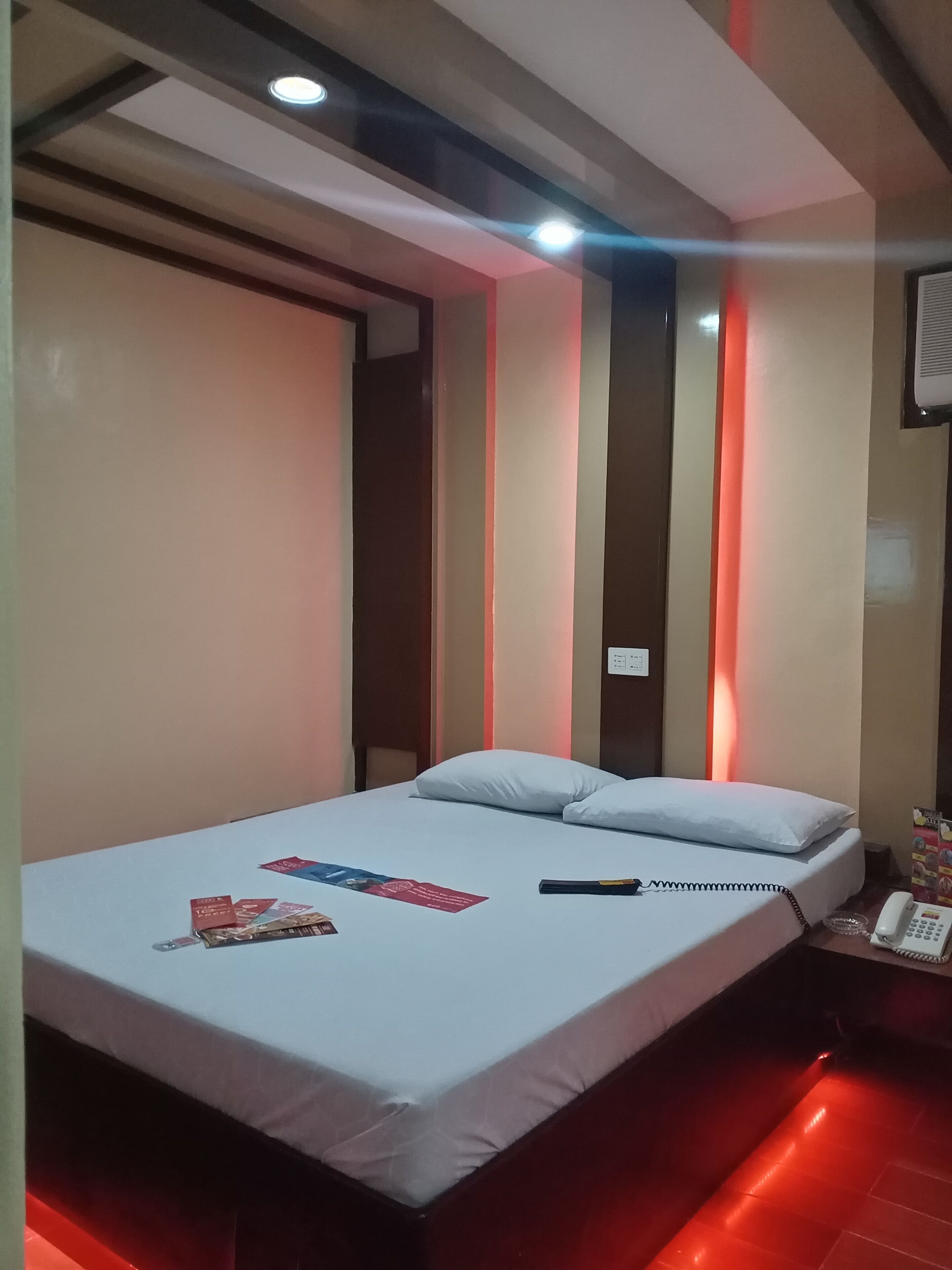 A hotel room with a bed, pillows, a bedside table with a phone, and a wall-mounted light fixture.