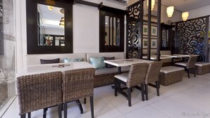 Um restaurante com interior moderno, apresentando uma área de estar com mesas e cadeiras de vime, um painel decorativo e aparelhos de ar condicionado fixados na parede.