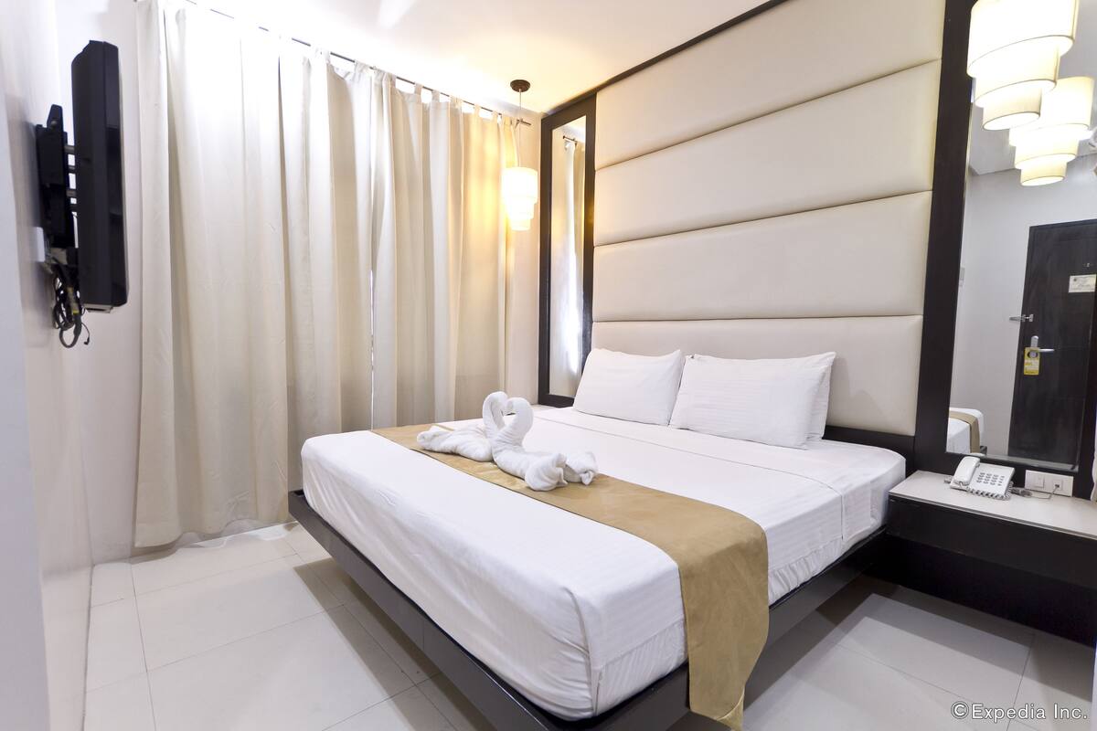 A hotel room with a large bed, a bedside table with a phone, and a mirror.