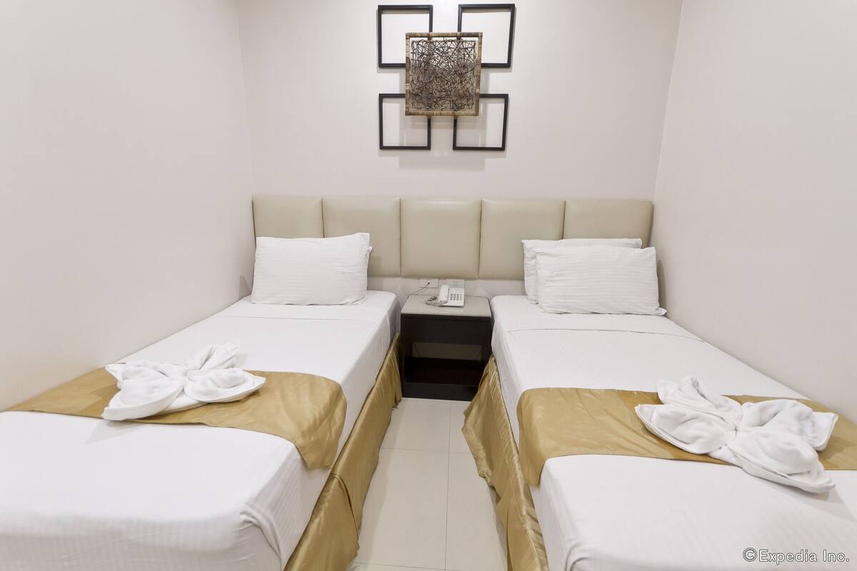 A hotel room with two single beds, a bedside table with a phone, and a wall-mounted artwork.