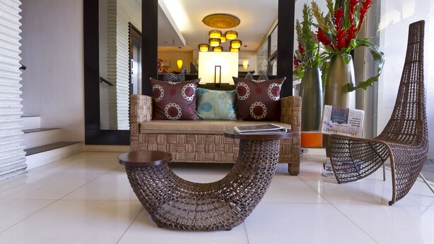 Um hall moderno com um sofá, cadeiras de vime, uma mesa de centro trançada e vasos decorativos.
