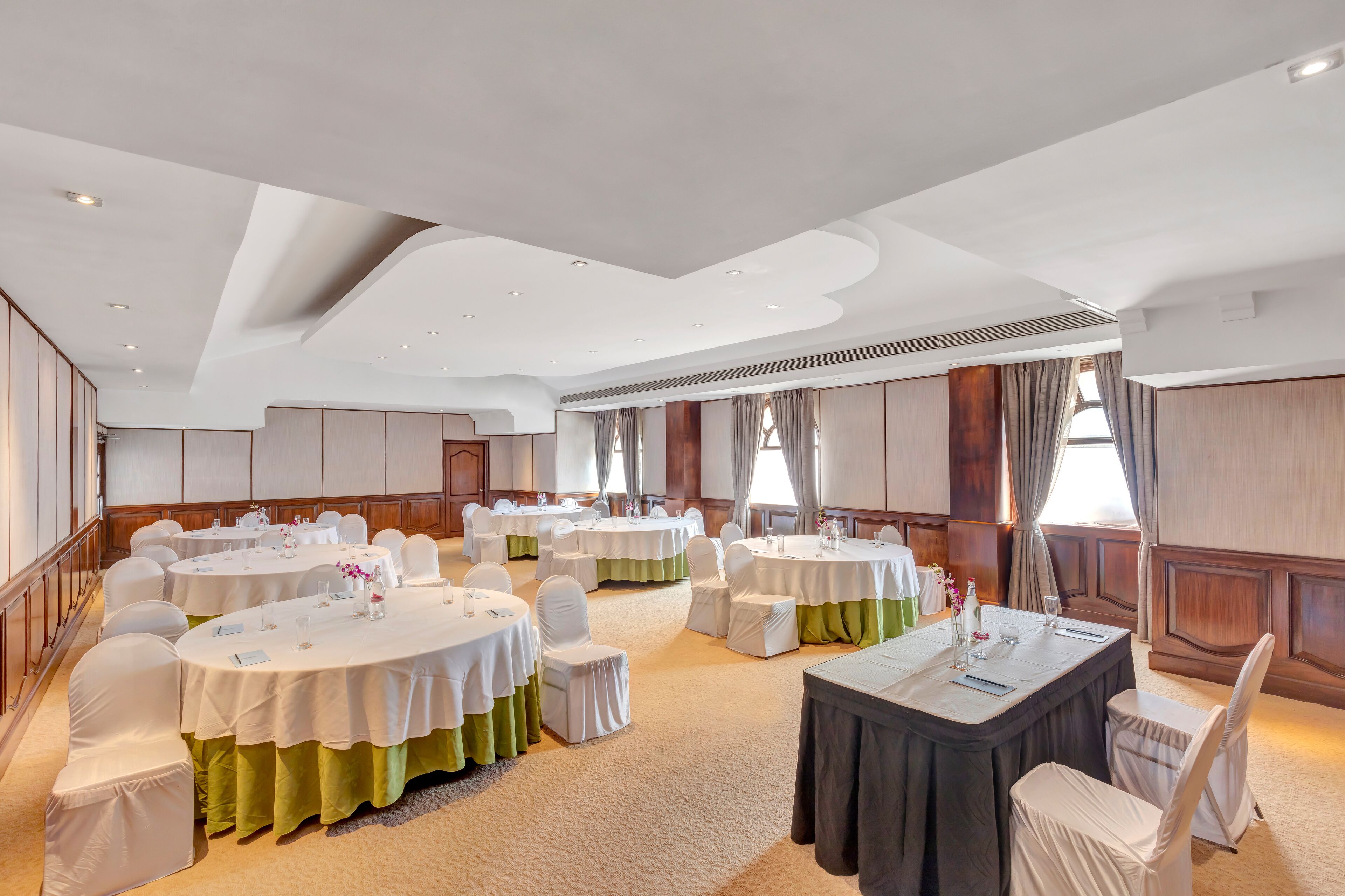 A conference room with multiple round tables, white chairs, and green tablecloths.