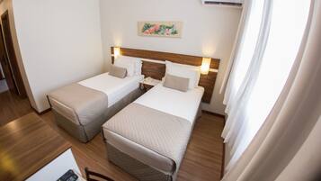 Quarto de hotel com duas camas de solteiro, uma cabeceira de madeira, uma mesinha com um controle remoto e um quadro na parede.