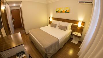 Una habitación de hotel con una cama grande, mesitas de noche, un escritorio y un equipo de aire acondicionado.