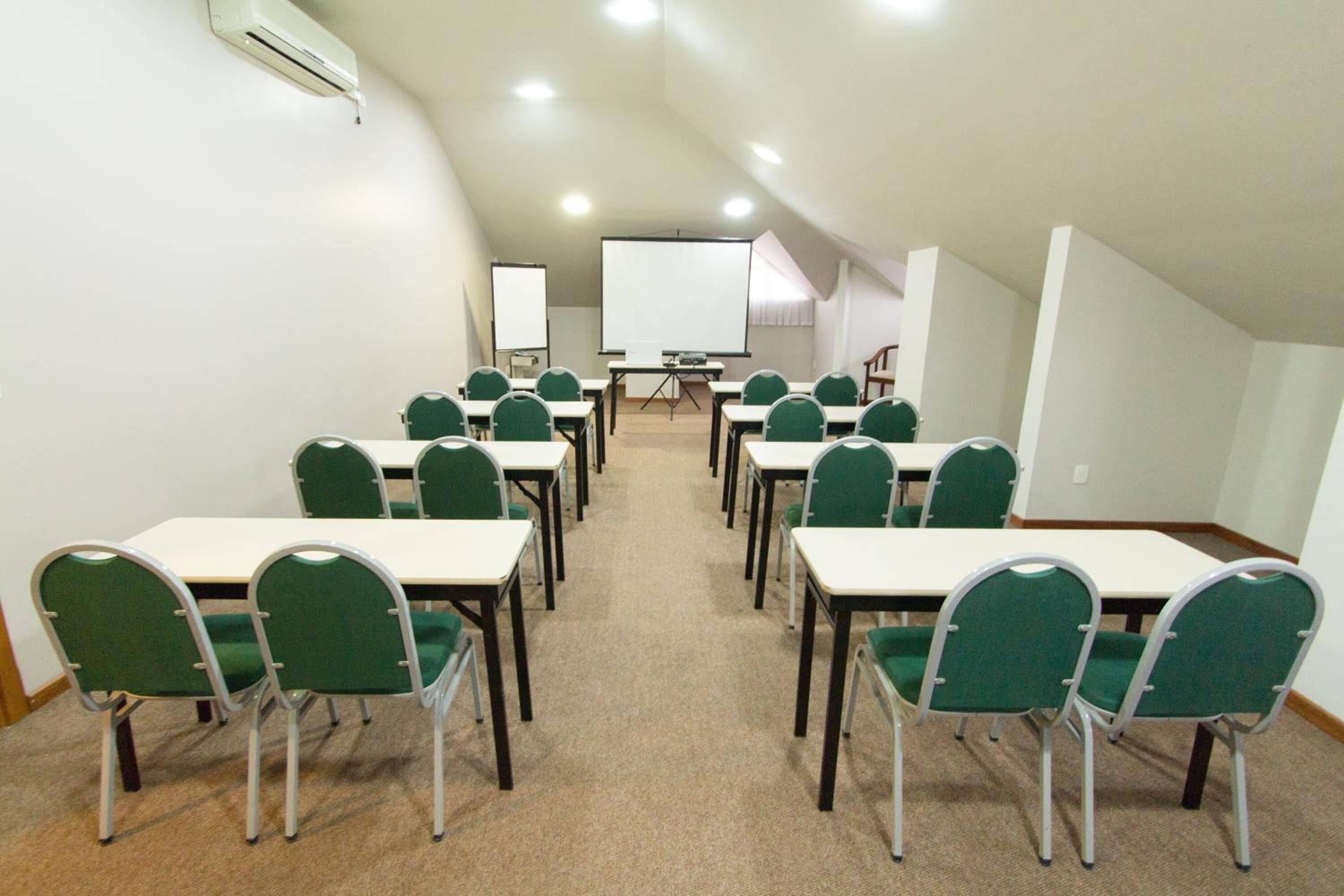 Un salón de conferencias con sillas verdes y mesas blancas, una pizarra y una pantalla de proyector.