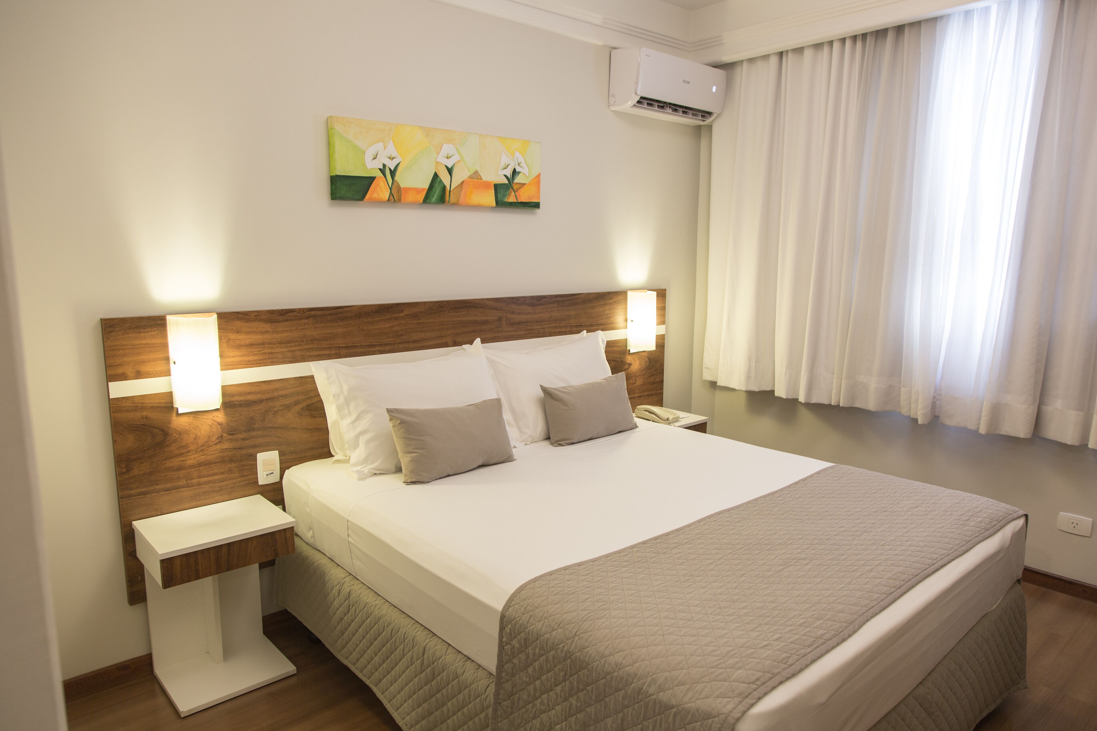 Una cama bien hecha con cabecera de madera, una mesita de noche y un aire acondicionado instalado en la pared.