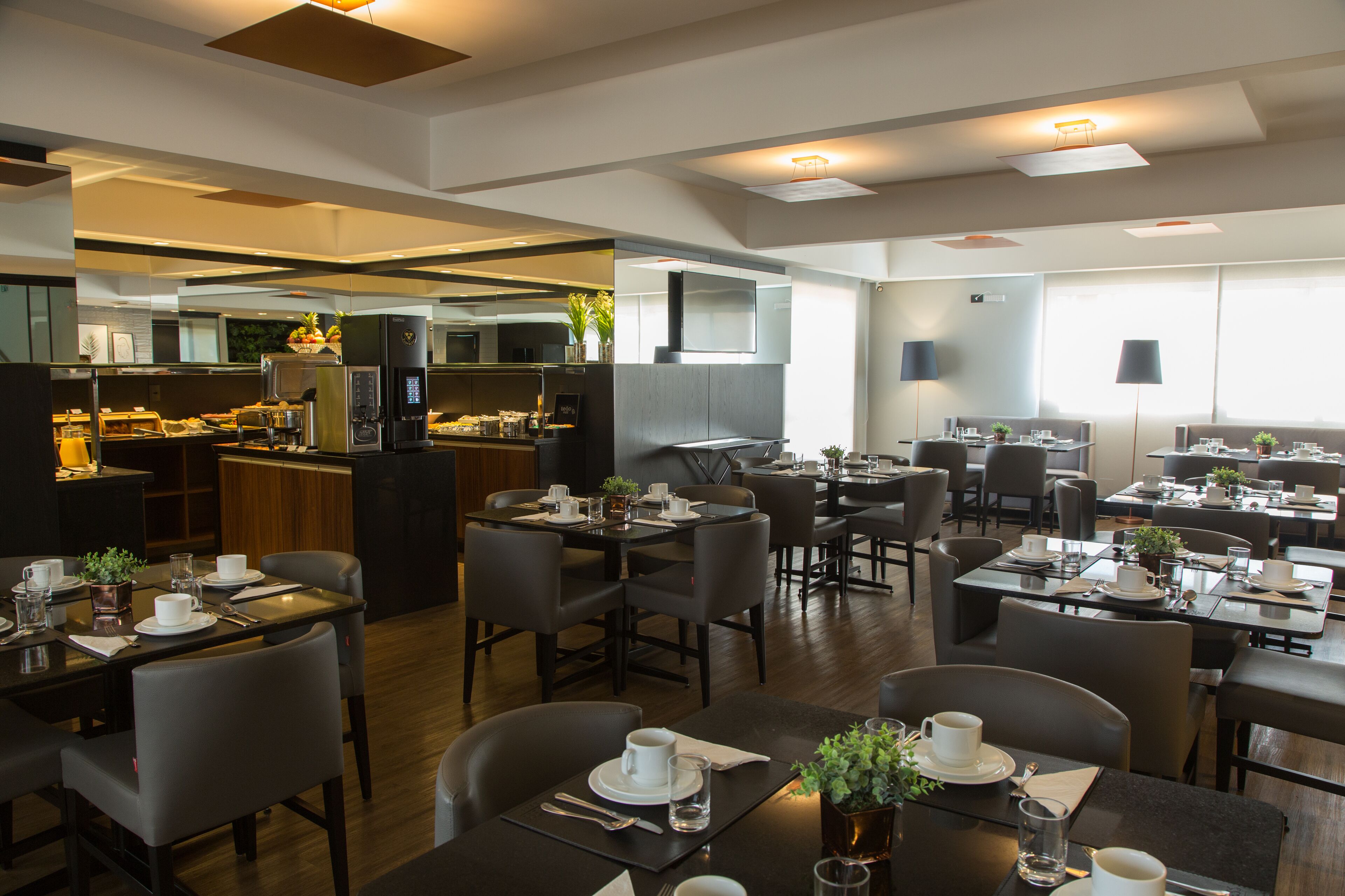 A modern dining area with multiple tables and chairs, a kitchen in the background, and a clean, well-lit environment.