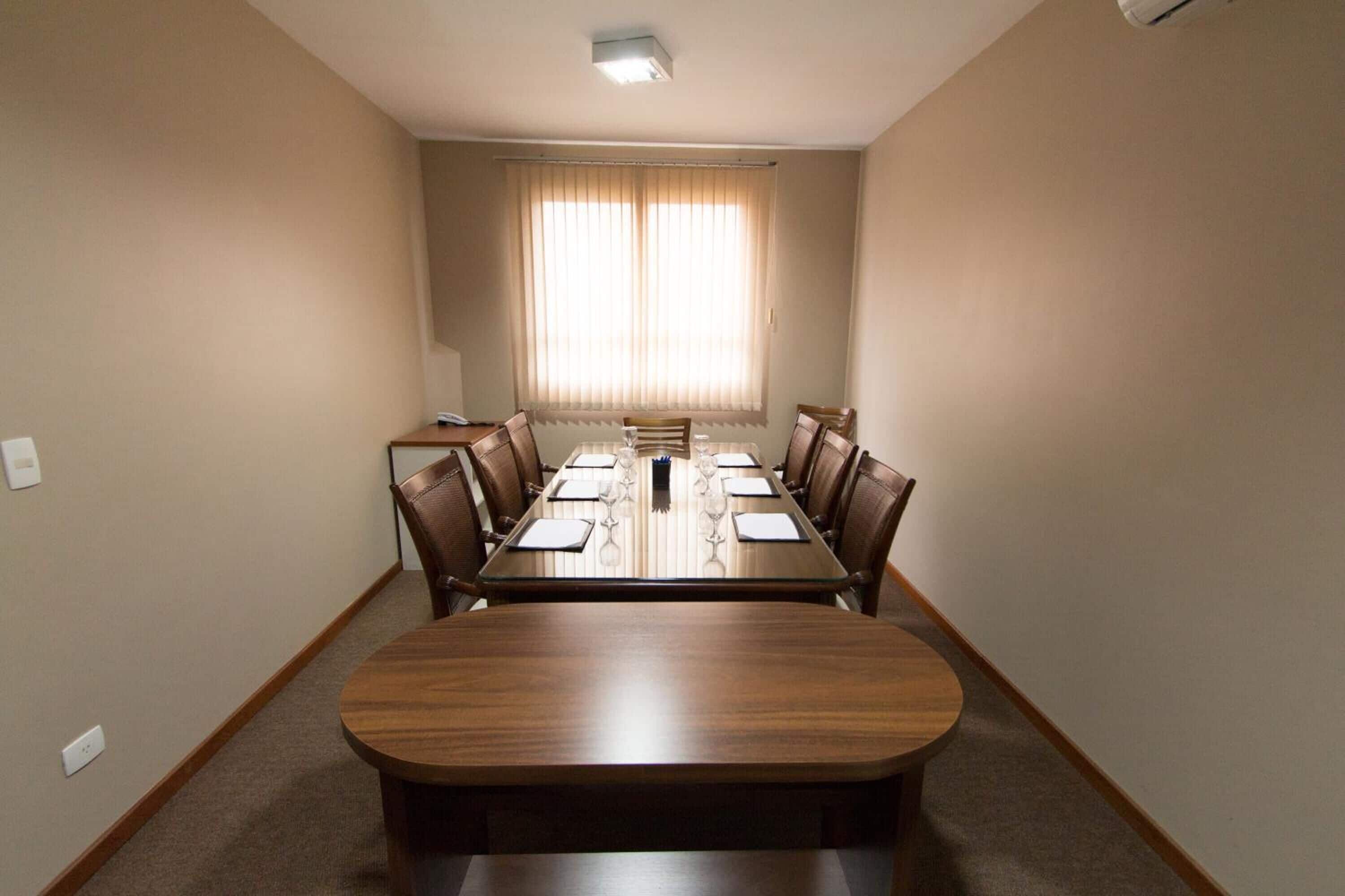 Une salle de conférence avec une longue table, des chaises et une fenêtre avec des rideaux.