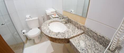 Une salle de bain avec des toilettes blanches, un lavabo doté d’un plan de travail en granit et un miroir au-dessus du lavabo.