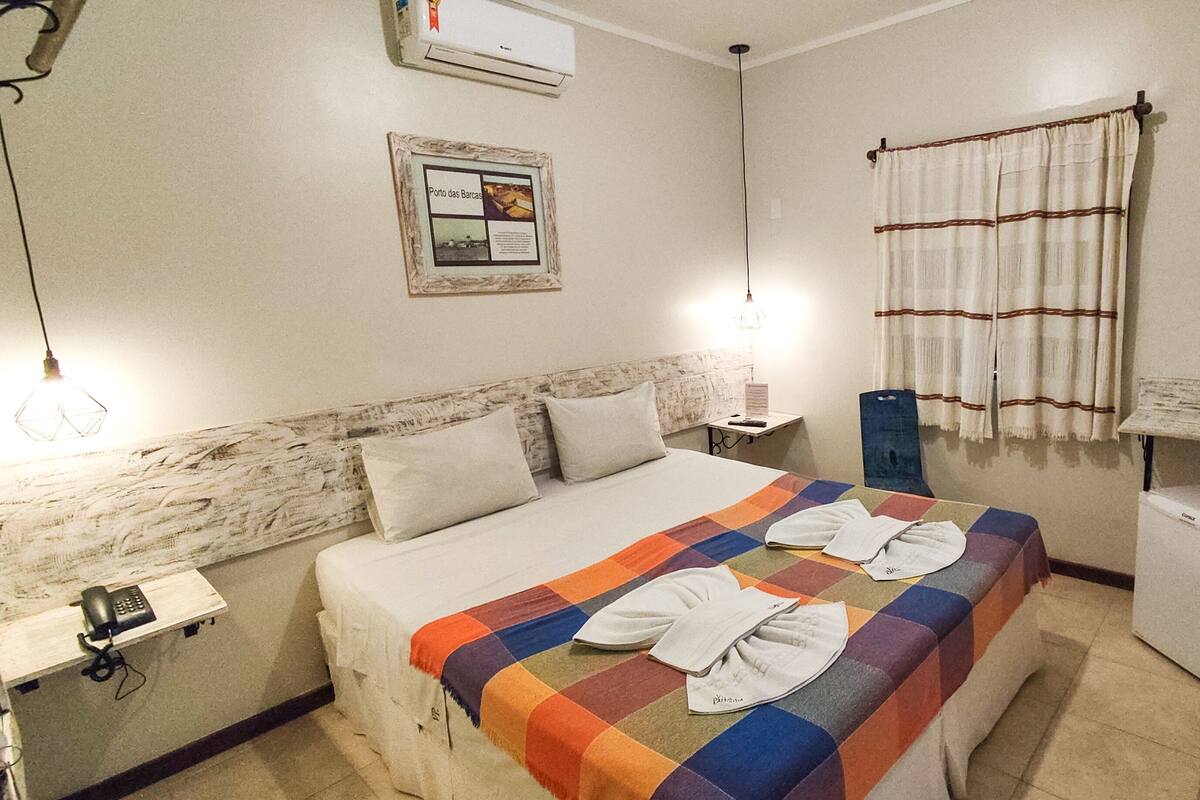 A hotel room with a bed, a small desk, a telephone, and a wall-mounted air conditioner.