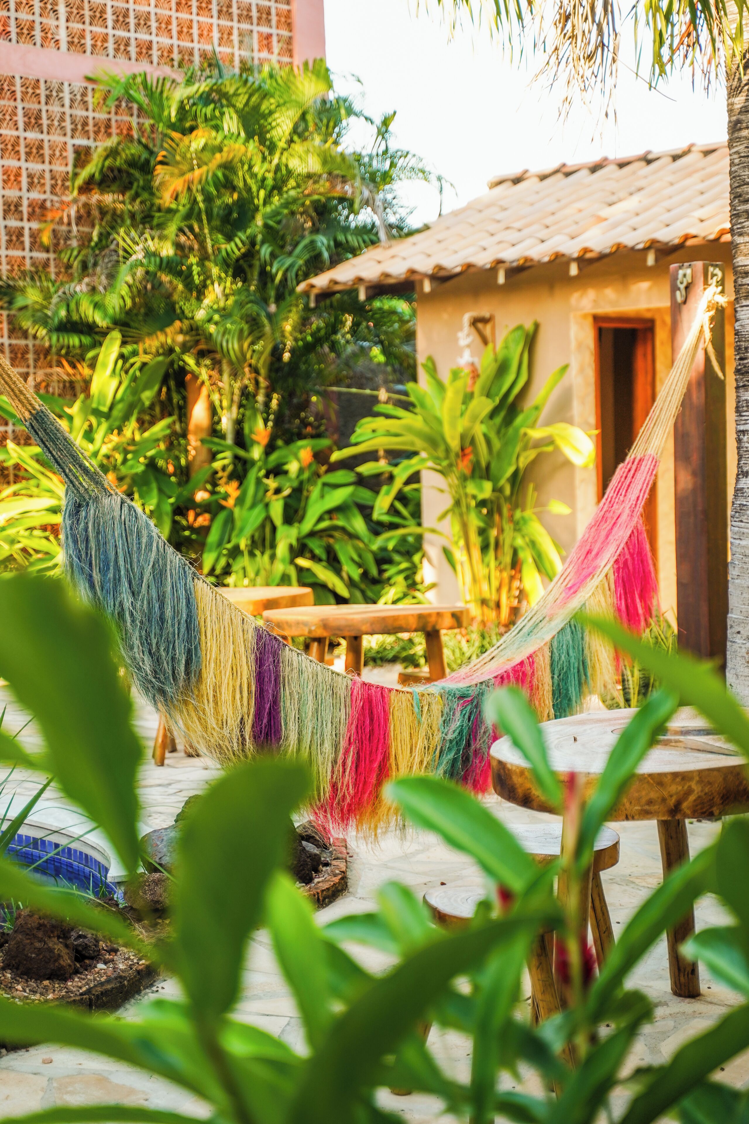 A hammock strung between trees in a garden area with a wooden table and a small building in the background.