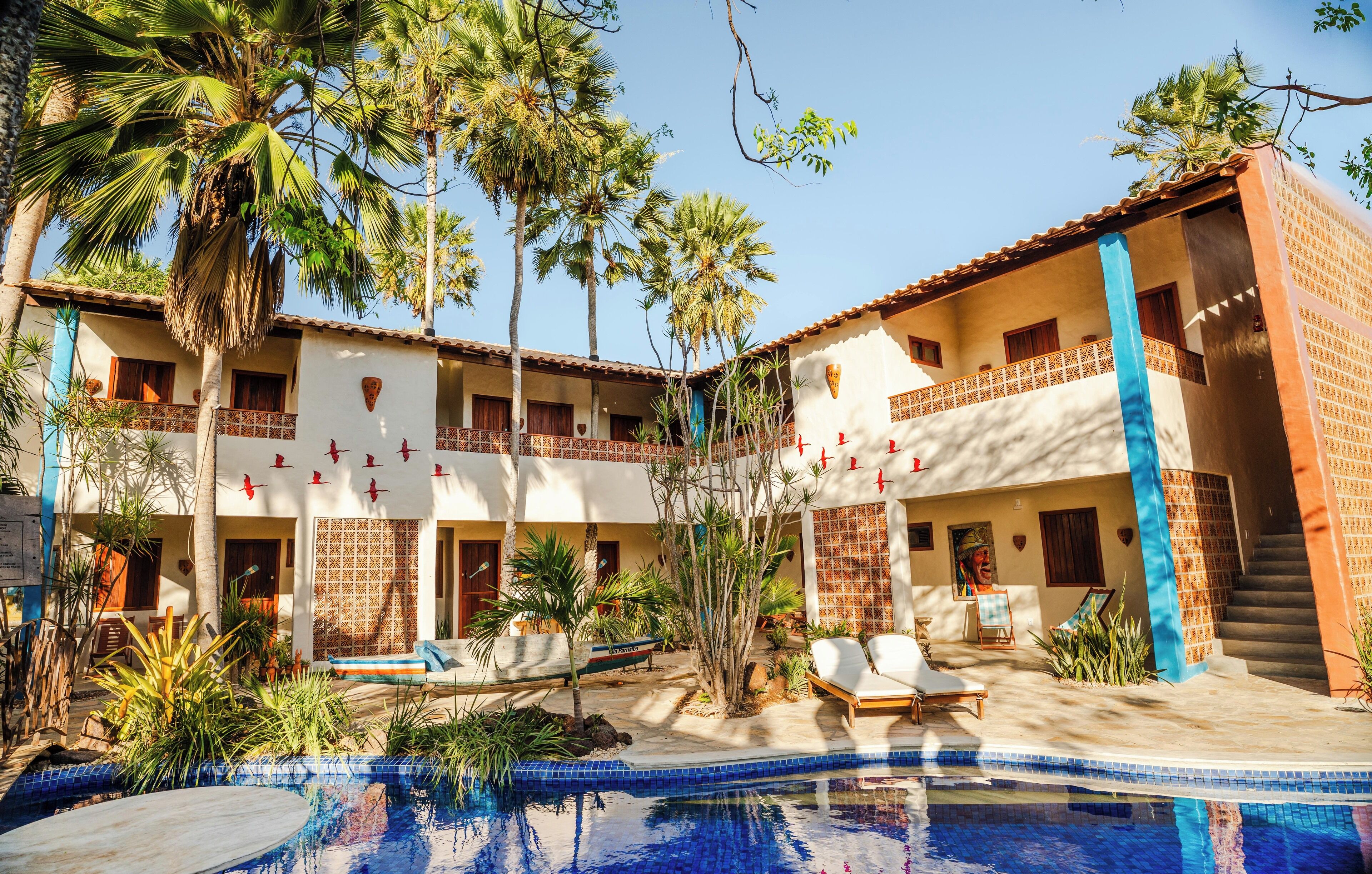 A two-story building with a swimming pool, palm trees, and outdoor seating.