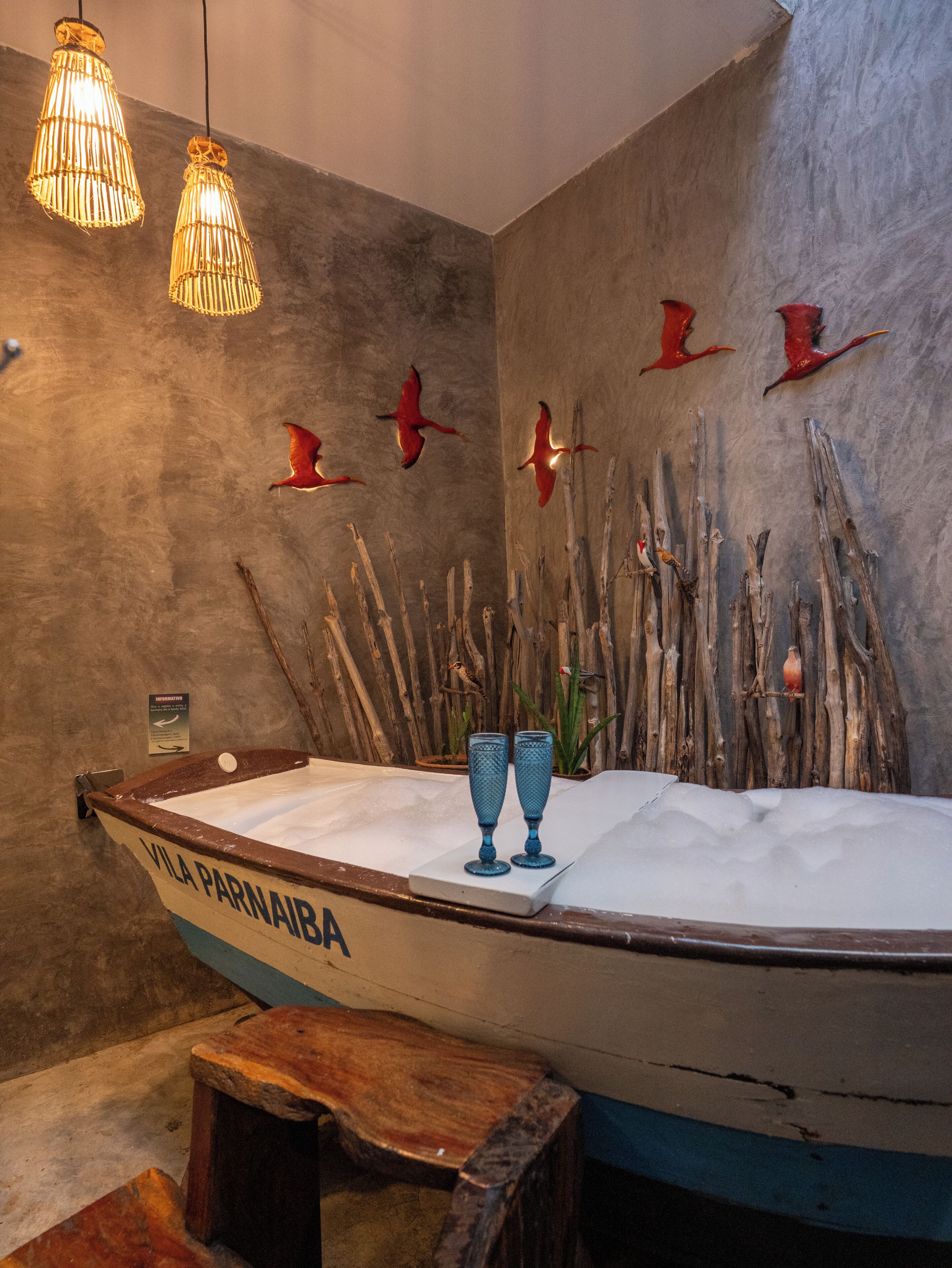 A boat-shaped bathtub with two blue glass vases on a wooden stool.