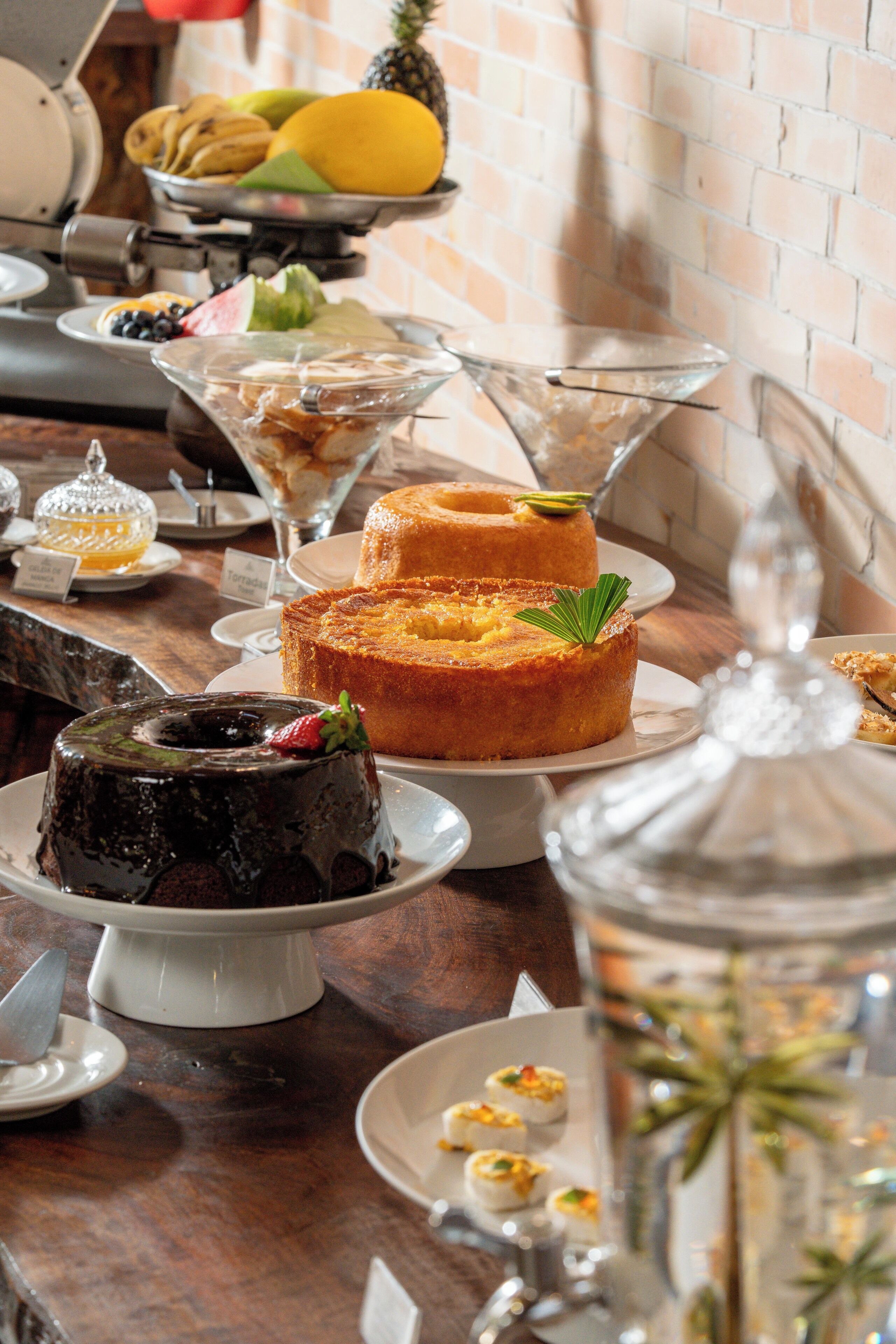 Een dessertbuffet met verschillende taarten en gebak, een fruitschaal en een glazen vaas met een plant.