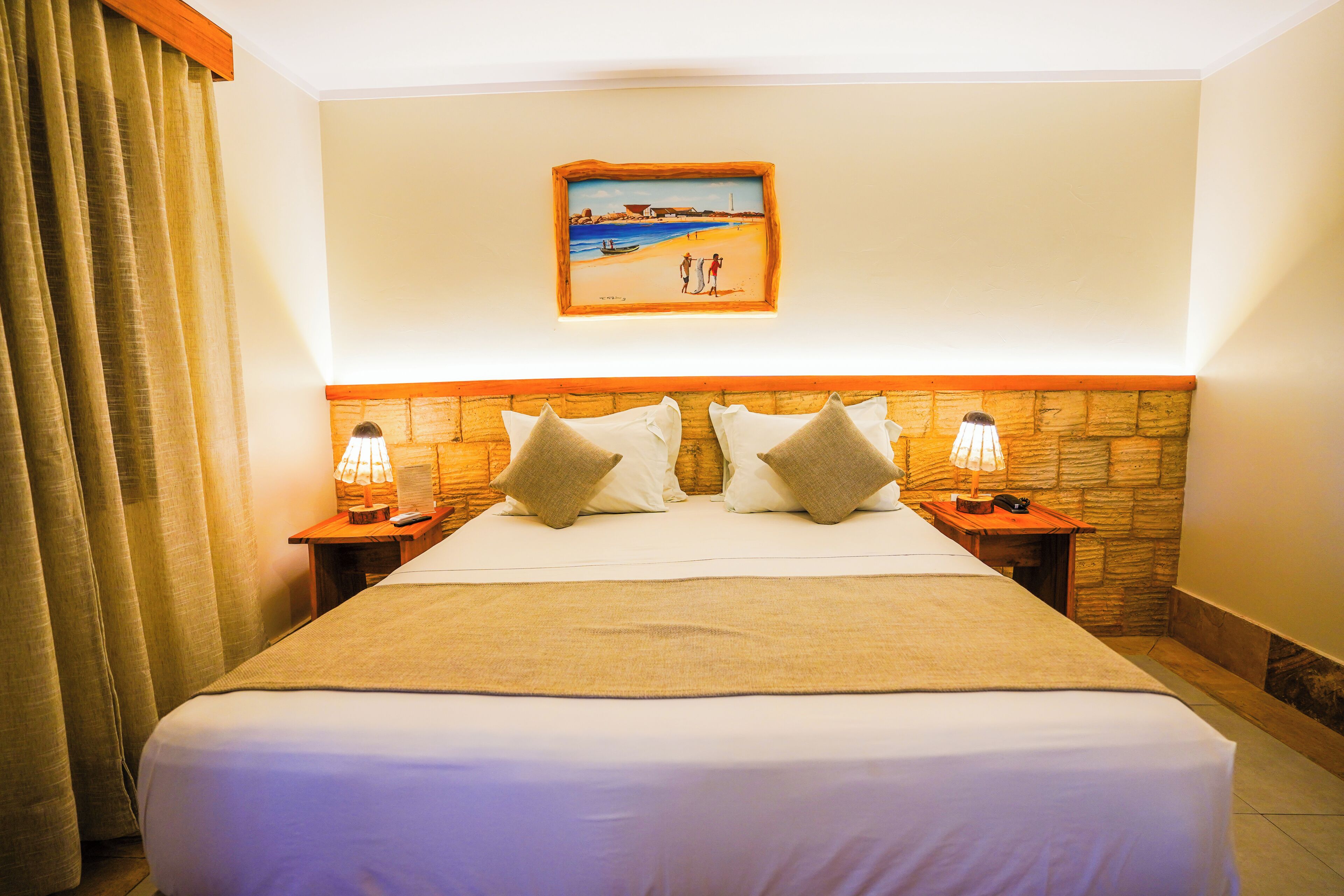 Ein Hotelzimmer mit einem großen Bett, zwei Nachttischlampen, einem Bild an der Wand und einem Holzkopfteil.