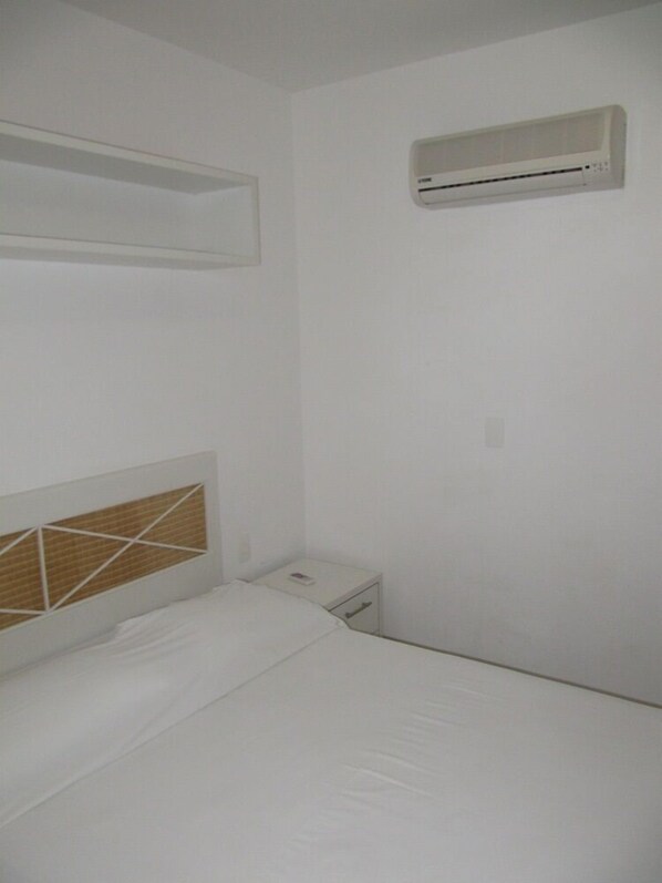 Una habitación pequeña con una cama individual, cabecera de madera, mesita de noche y aire acondicionado instalado en la pared.