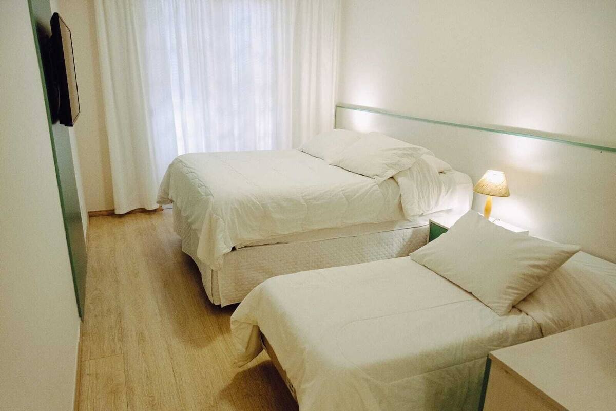 Una habitación de hotel con dos camas individuales, una lámpara de noche y una ventana con cortinas.