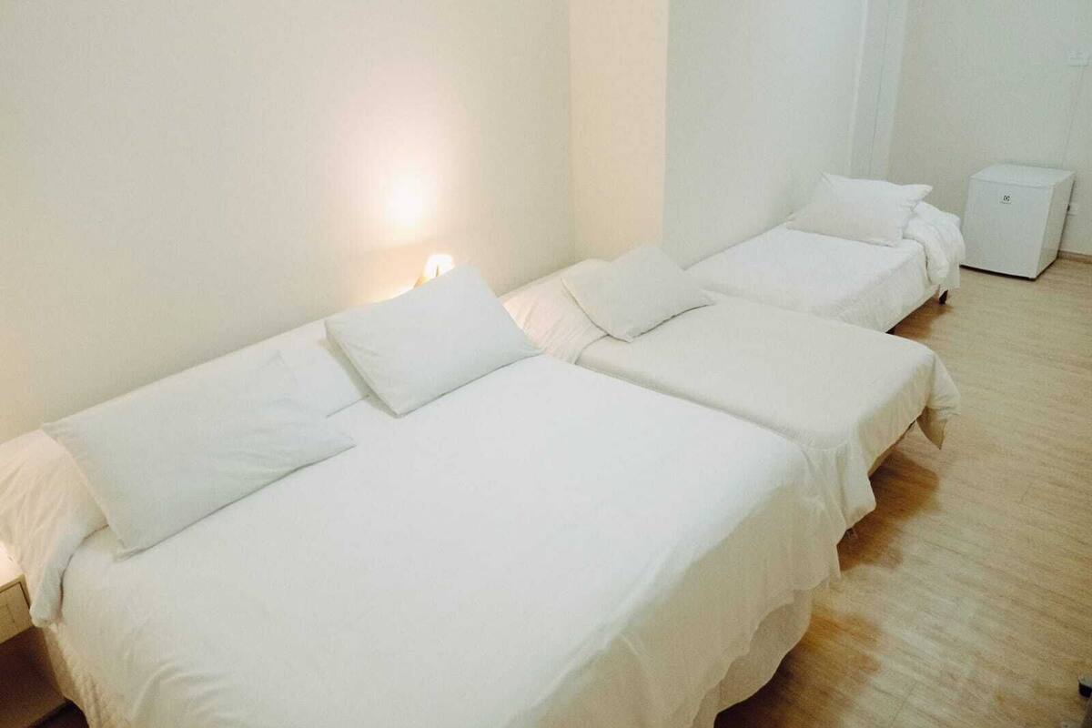 Habitación de hotel con dos camas individuales, una mesita de noche, una lámpara de noche pequeña y un armario blanco.
