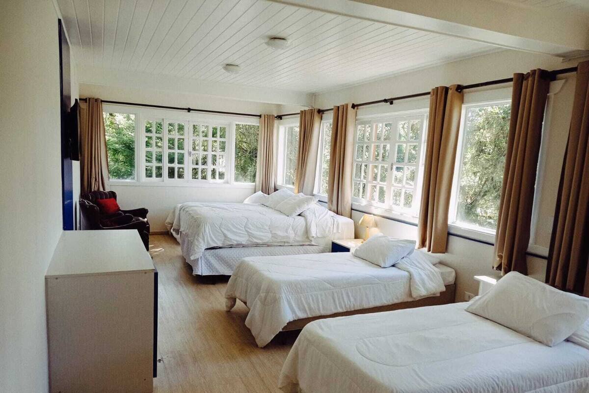 Una habitación con tres camas, un escritorio y ventanas grandes con cortinas.