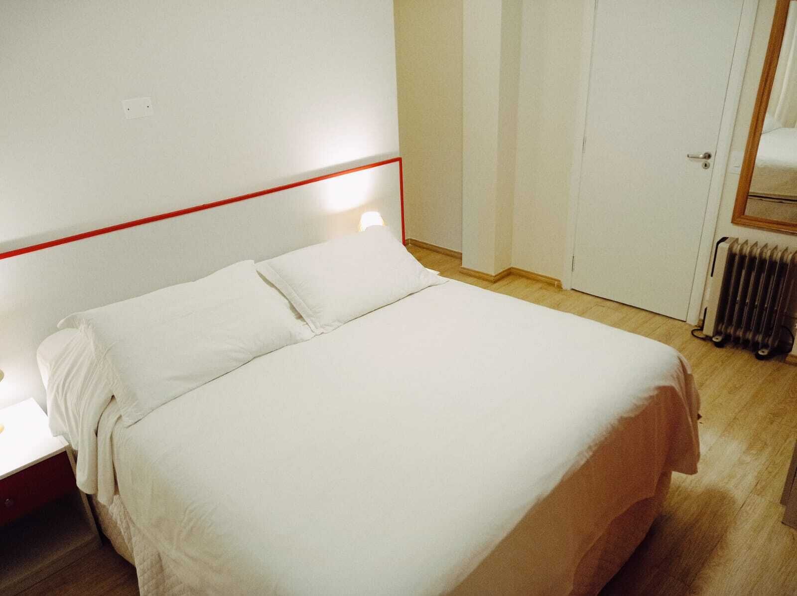 Een bed met witte beddengoed in een kamer met een houten vloer en een witte deur.