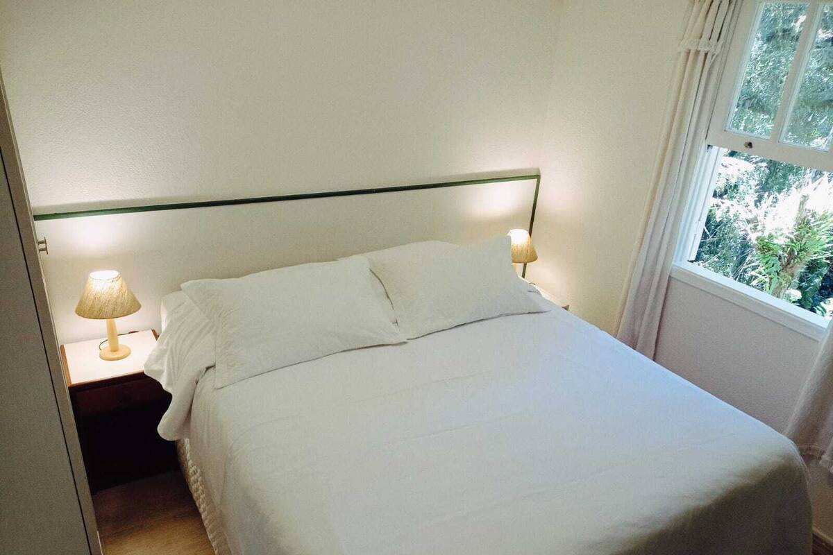 Una cama con sábanas blancas y bien tendidas en una habitación de diseño limpio y sencillo. Hay dos lámparas de noche a ambos lados de la cama.