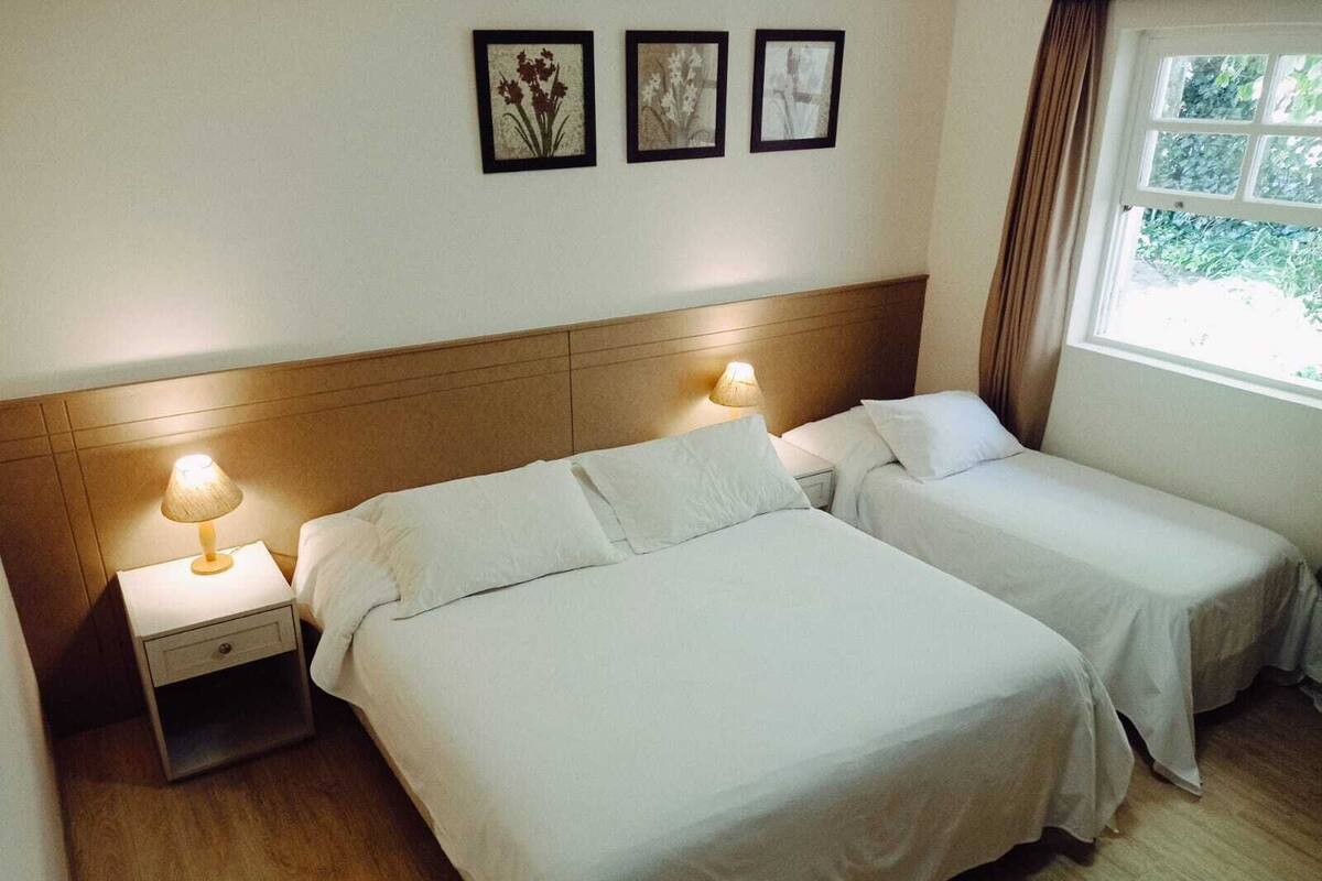 Una habitación de hotel con dos camas, una mesita de noche con lámpara y tres cuadros en la pared.