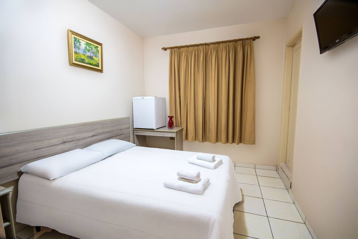 Ein Hotelzimmer mit Bett, Schreibtisch, Fernseher und einem Fenster mit Vorhängen.