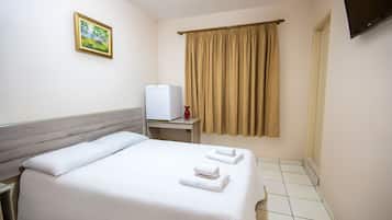 Una habitación de hotel con cama, escritorio, televisor y ventana con cortinas.