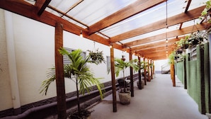 Un pasillo cubierto con vigas de madera, plantas en macetas y suelo de hormigón.