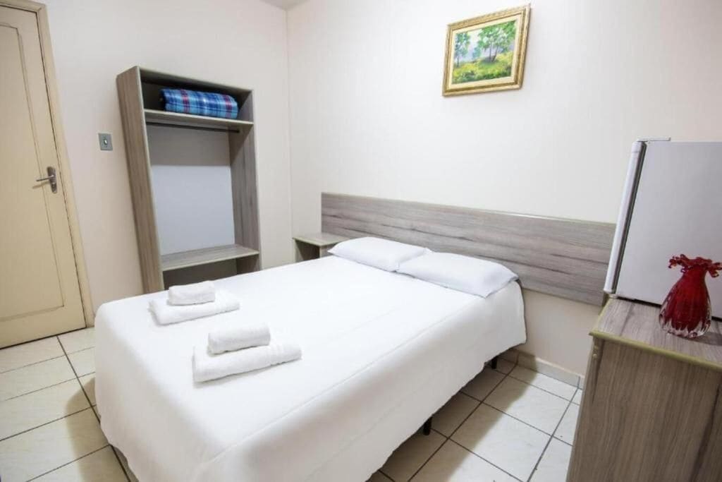 A hotel room with a bed, a wardrobe, a nightstand, and a painting on the wall.