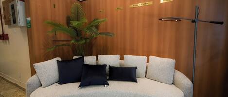 A curved sofa with multiple cushions in a lobby area with wooden paneling and a plant.