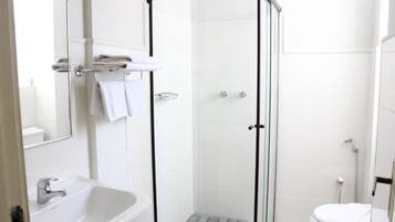 Un baño moderno con ducha de vidrio, lavamanos blanco y retrete.