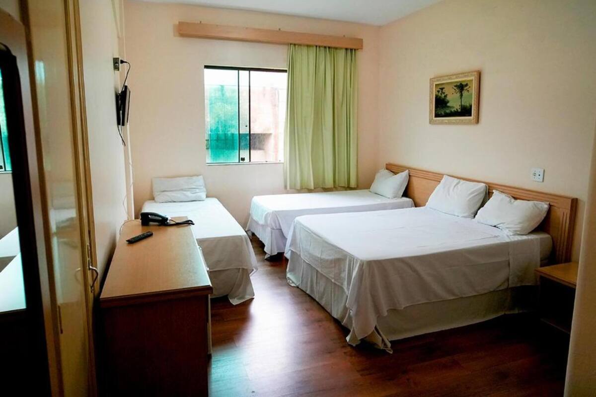 Ein Hotelzimmer mit zwei Einzelbetten, einem Holztisch, einem kleinen Tischchen, einem Fenster mit Blick und einem Bild an der Wand.
