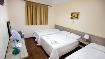 Habitación de hotel con dos camas, un escritorio con ventilador, un cuadro en la pared y una ventana con cortinas.