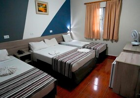 Una habitación de hotel con dos camas individuales, un escritorio con un ventilador y una ventana con cortinas.