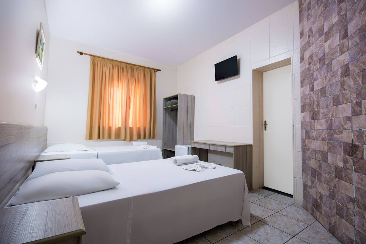 Ein Hotelzimmer mit zwei Betten, einem Schreibtisch, einem Fernseher und einem Kleiderschrank.