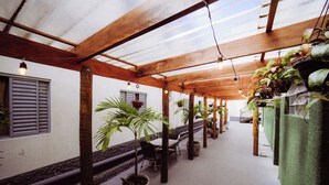 Un espacio de estar al aire libre cubierto con vigas de madera, plantas en macetas y suelo de concreto.