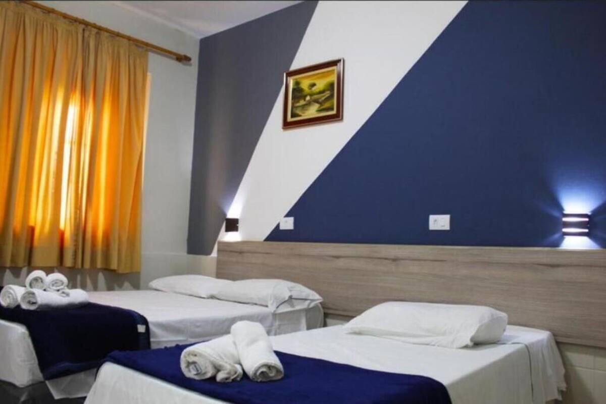 Ein Hotelzimmer mit drei Einzelbetten, jedes mit einem zusammengerollten Handtuch und einer blauen Decke.