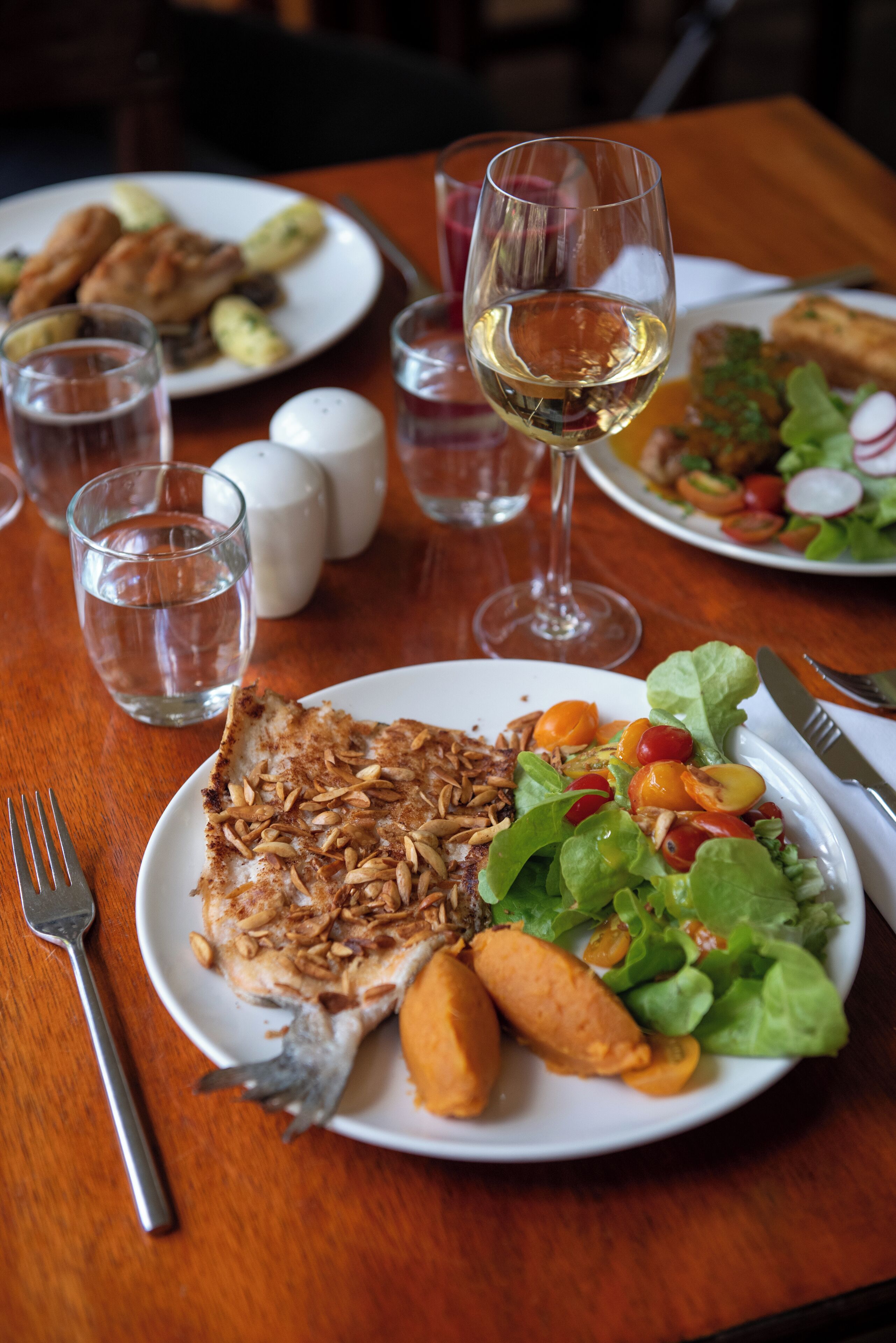 A dining table with plates of food, glasses of water and wine, and salt and pepper shakers.