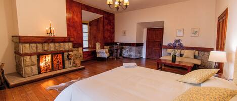 Un dormitorio espacioso con una cama grande, una chimenea de piedra, piso de madera y un candelabro.