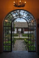 Una entrada en arco con vistas a un jardín, un camino de piedra y una casa tradicional al fondo.