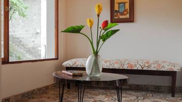 Una habitación con piso de baldosas estampadas, una mesa redonda con un florero, un banco y una ventana con vista a follaje.