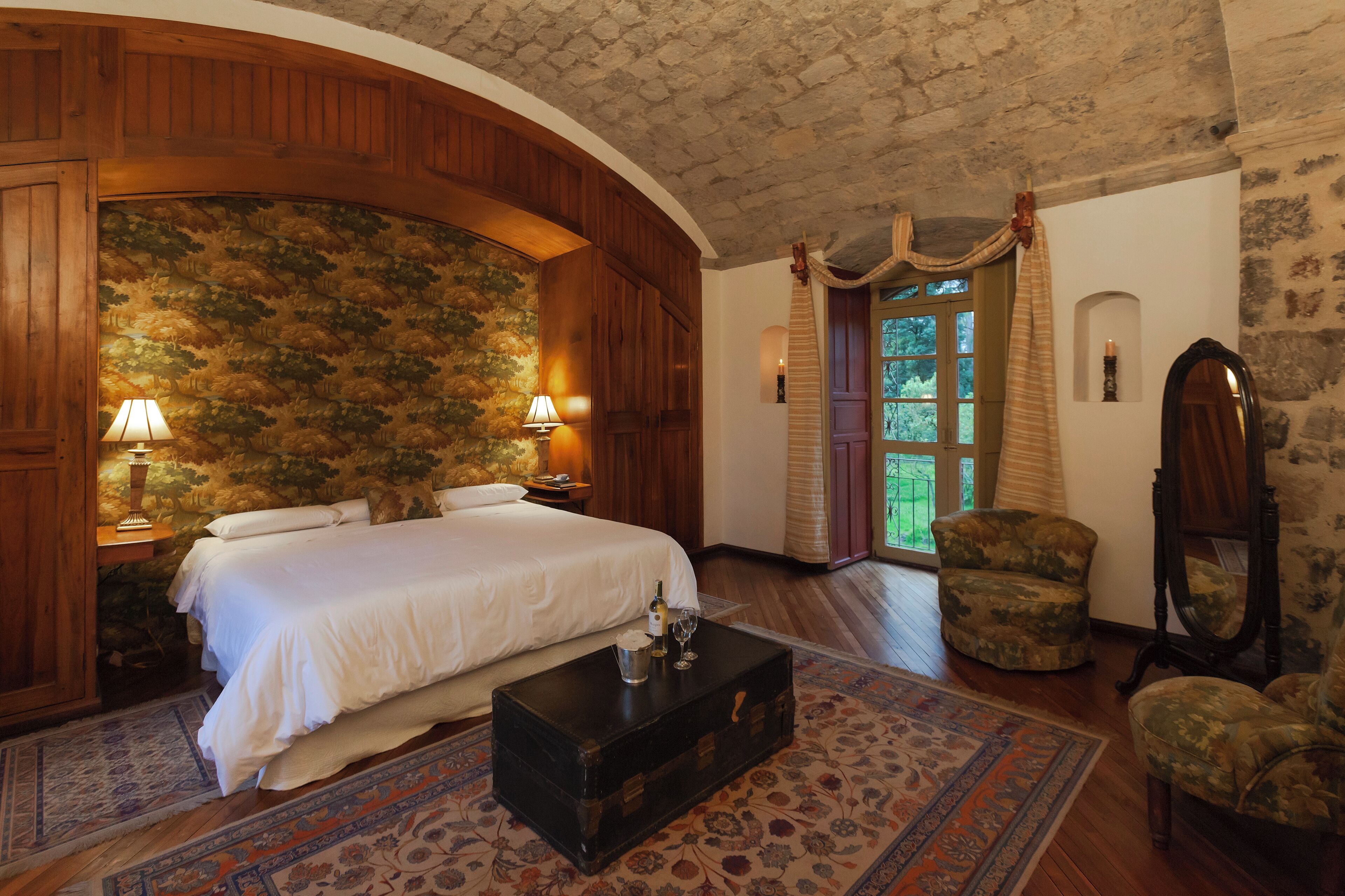Un dormitorio con una cama grande, paneles de madera, techo de piedra y vistas a la vegetación por una ventana.