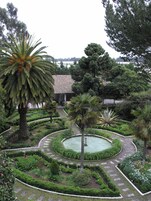 Un jardín con un estanque circular, palmeras y un edificio con techo de tejas.