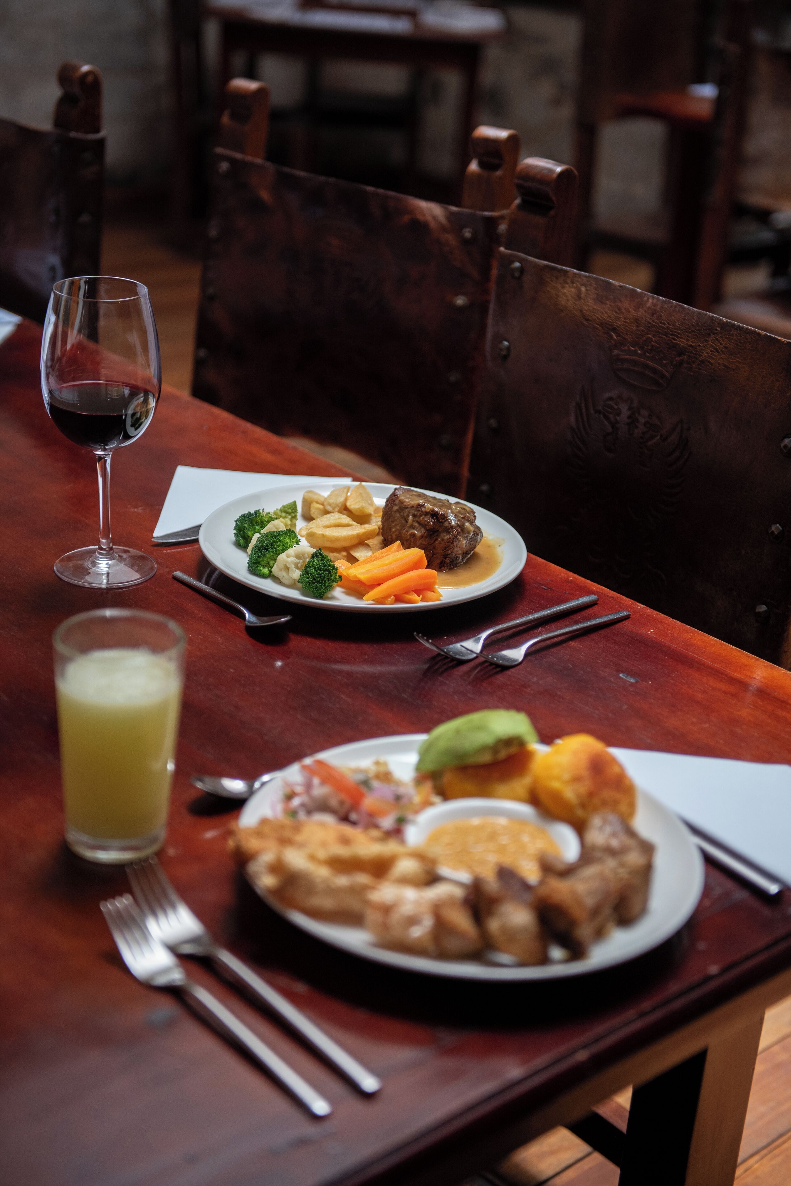 A wooden dining table with plates of food, cutlery, and a glass of juice.