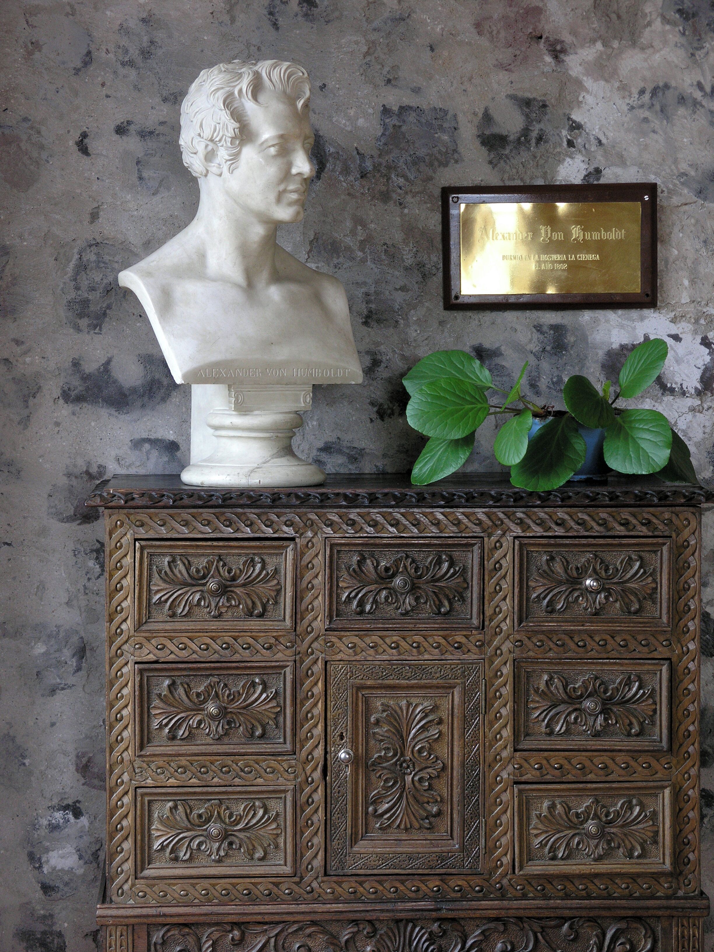 A bust sculpture on a cabinet with ornate carvings and a plaque.